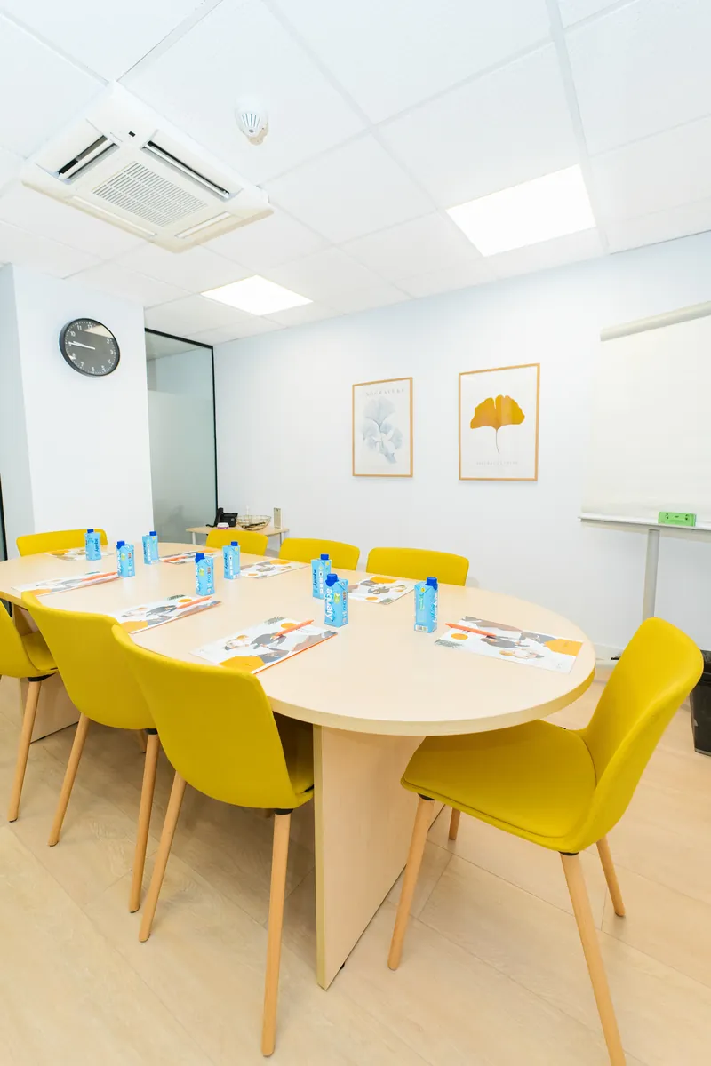 Sala de reuniones con mesa ovalada, sillas amarillas y pantalla en CN Centros de Negocios