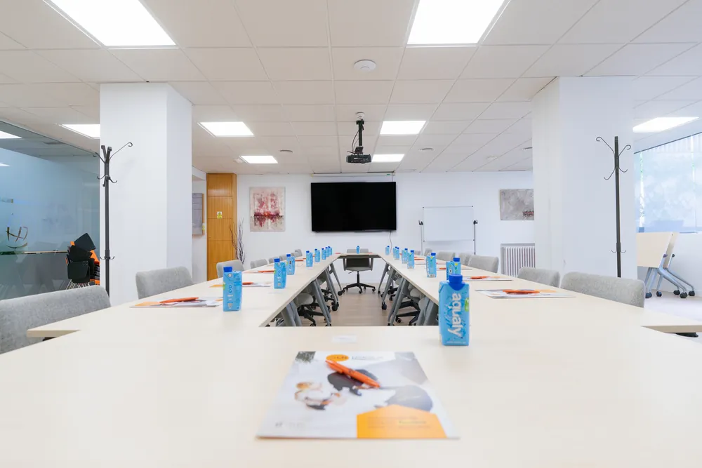 Sala de formación y eventos con mesas en hilera y pantalla en CN Centros de Negocios